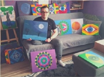 Tomasz Włodarczyk na kanapie z obrazami.