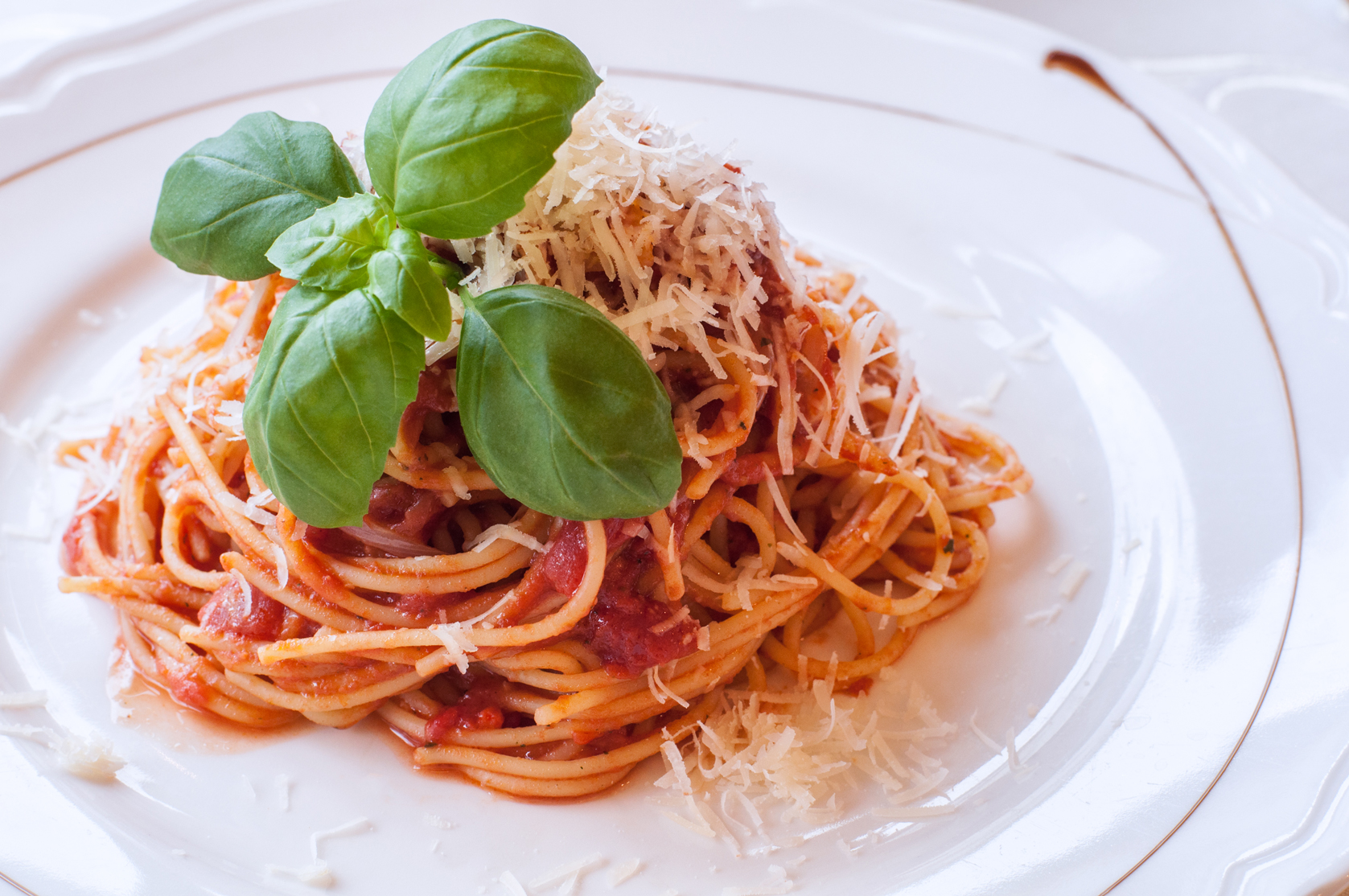 Zdjęcie makaronu z sosem pomidorowym udekorowany listkmi bazylii.