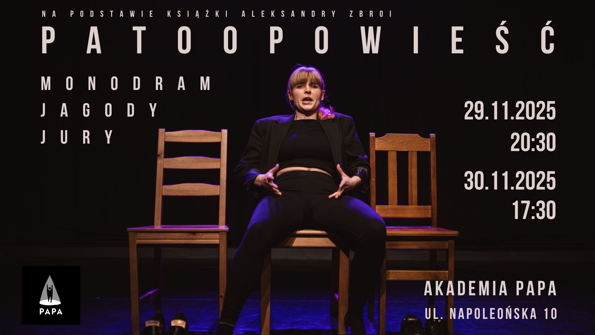 Kobieta w jasnych włosach z grzywką. Ubrana na czarno. Siedzi na jednym z trzech krzeseł, na środku. Z góry świeci na nią różowe światło. Tło jest ciemne.