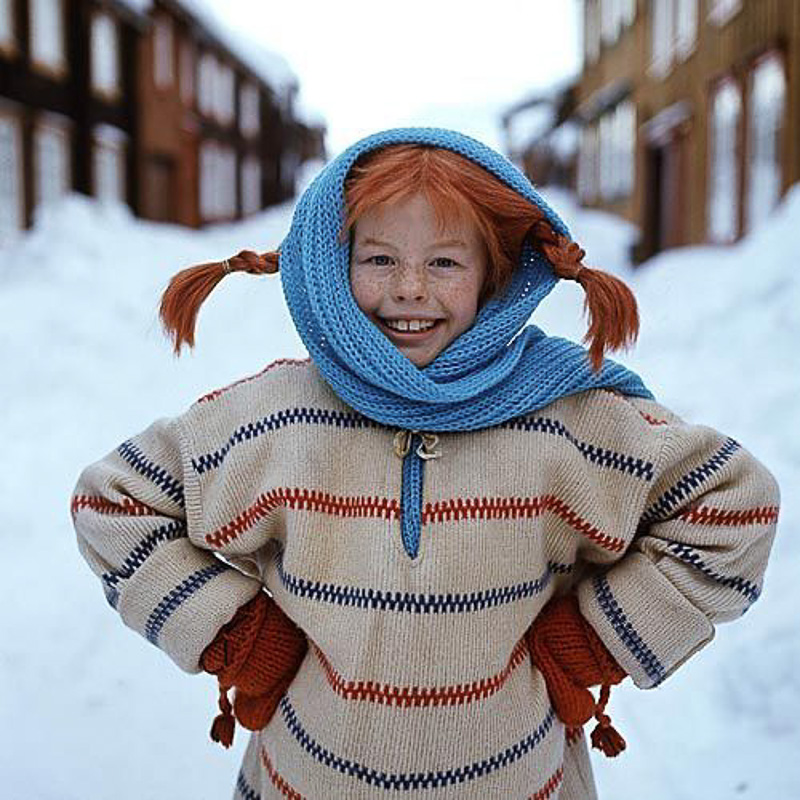 Dziewczynka w rudych warkoczykach z niebieksim szalikiem. Za nią ulica pełna śniegu.