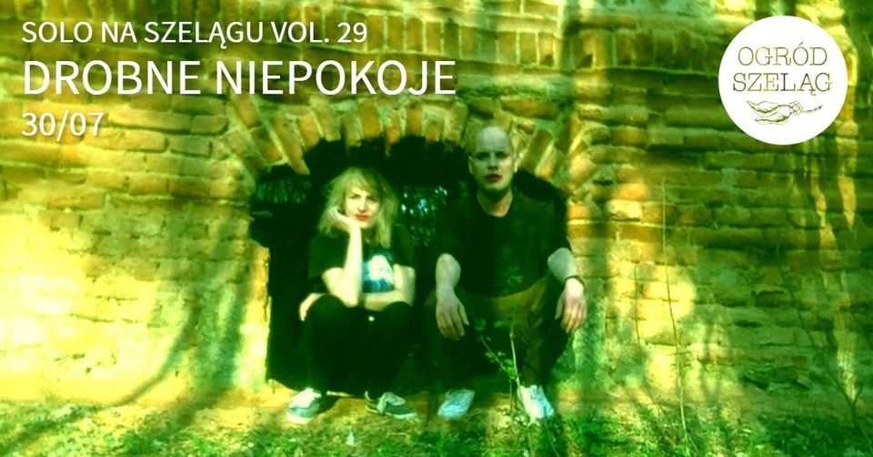 Kobieta i mężczyzna kucają przy murze. Mają pomalowane na czerwono usta.