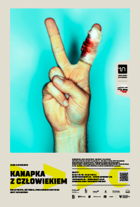 Na plakacie dłoń z dwoma palcami ułożonymi w literę V, jeden z palców zabandażowany i pobrudzony krwią. U dołu plakatu informacje o spektaklu.