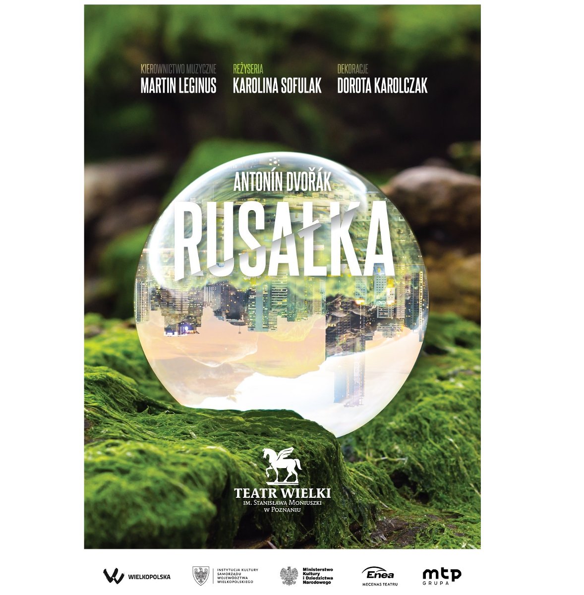 Na zielonym mchu leży szklana kula, w której odbija się obraz fragmentu miasta z drapaczami chmur odwrócony o 180 stopni. Na kupi i ponad nią białe napisy z informacjami o spektaklu.