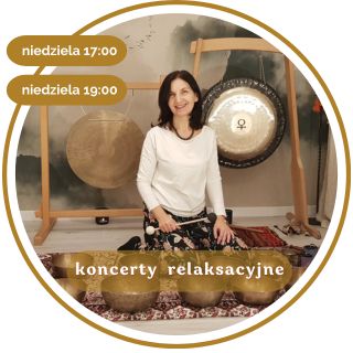 Kobieta w średnim wieku z czarnymi włosami. Ubrana w biały długi rękaw i wzorzyste spodnie. Siedzi na podłodze pokrytej dywanami. Za nią wiszą 2 gongi. Przed nią leży kilka mis.