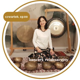 Kobieta w średnim wieku z czarnymi włosami. Ubrana w biały długi rękaw i wzorzyste spodnie. Siedzi na podłodze pokrytej dywanami. Za nią wiszą 2 gongi. Przed nią leży kilka mis.