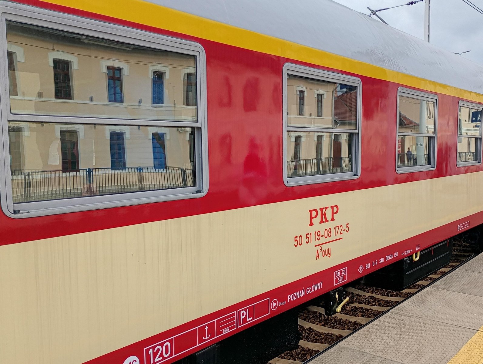 Biało-beżowy wagon starego składu pociagow PKP. Ma duże okna. Stoi na peronie.