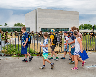 Grupa dzieci wchodzi na most, w tle widać prostopadłościenny, szary budynek Bramy Poznania.