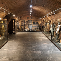 Pomieszczenie forteczne ze szklanymi gablotami po obu stronach i na wprost, w gablotach manekiny i eksponaty