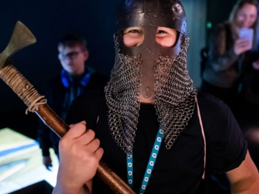 Osoba w wikińskim hełmie trzyma w obu dłoniach lekki toporek bojowy.