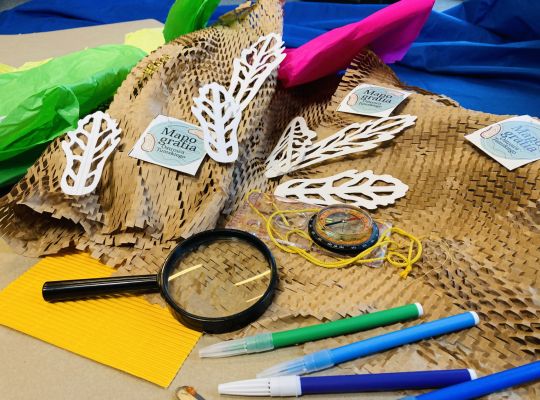 Na stole leżą różne przybory i akcesoria, w tym lupa i kolorowe mazaki.