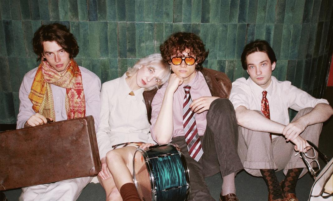 Kilka mlodych osób siedzi oparta o ścianę, oświetlona mocnym, białym światłem.