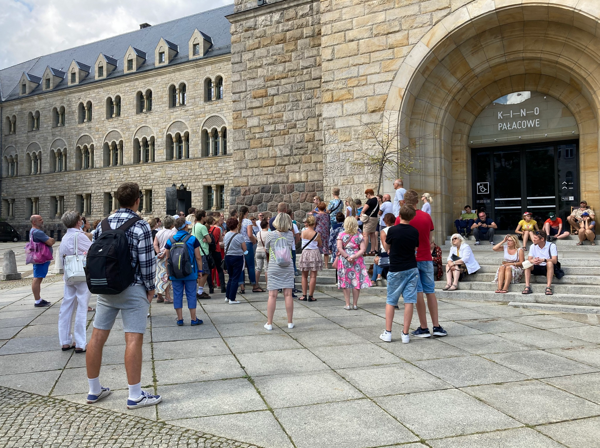 Grupa ludzi stoi pod wejściem do Kina Pałacowego w poznańskim Zamku Cesarskim.