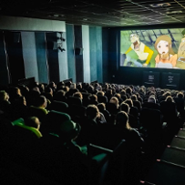 Publiczność festiwalowa ogląda film animowany w kinie Muza. W sali jest ciemno, głowy widzów oświetla jedynie światło z ekranu.