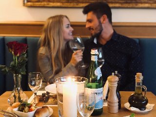 Zdjęcie, para siedzi przy zastawionym stole, świeca, kwiaty, butelka wina.