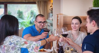 Zdjęcie, grupa osób siedzi przy wspólnym stole i stuka się kieliszkami z winem.