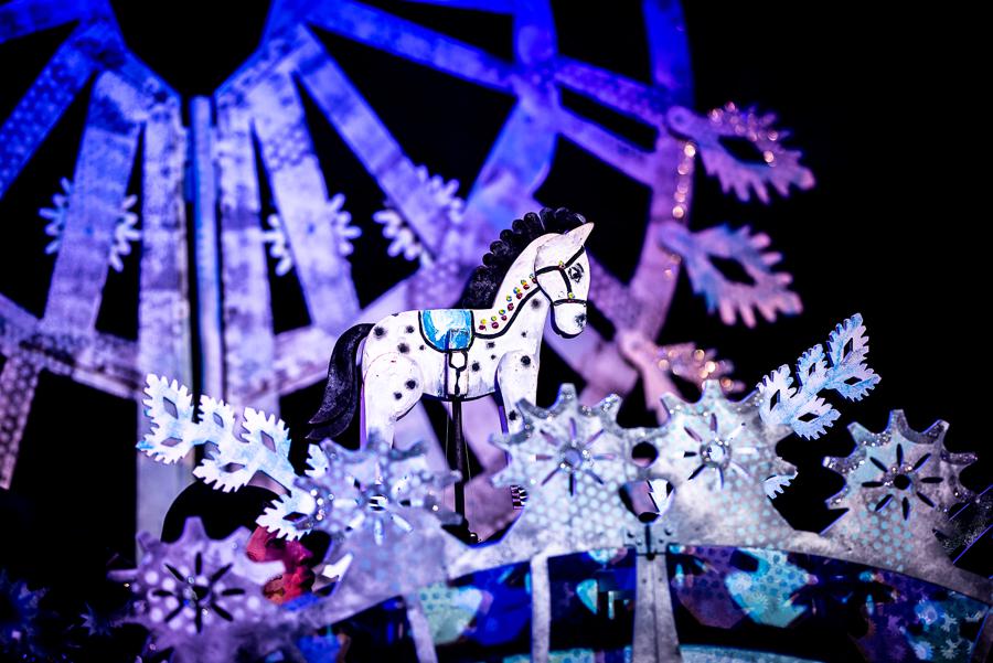 Zdjęcie ze spektaklu - biały drewniany konik wśród dekoracji w bialo-fioletowych kolorach.