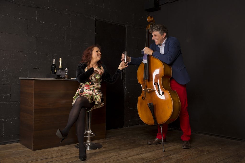 Zdjęcie ze spektaklu - kobieta siedzaca na stołku barowym, obok niej mężczyzna stojący przy kontrabasie.