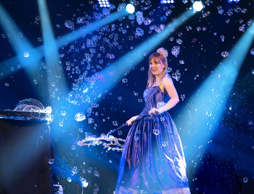 Zdjęcie z przedstawienia: kobieta w długiej, niebieskiej sukni wśród baniek mydlanych.