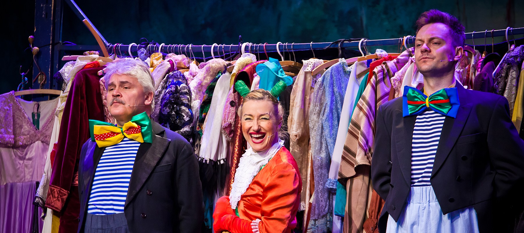 Zdjęcie ze spektaklu - aktorka w przebraniu do przedstawienia na tle wieszaka pełnego ubrań.