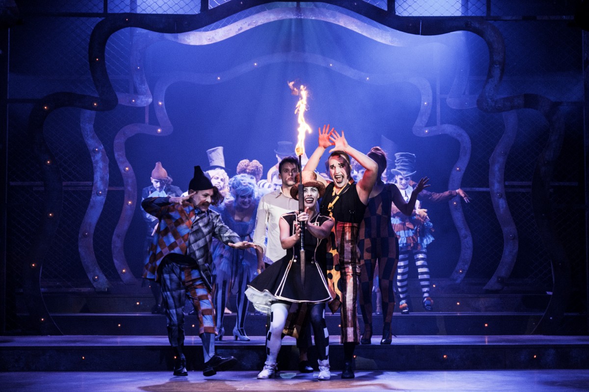 Zdjęcie ze spektaklu - grupa aktorów na scenie, na pierwszym planie aktorka trzymająca zapaloną pochodnię.