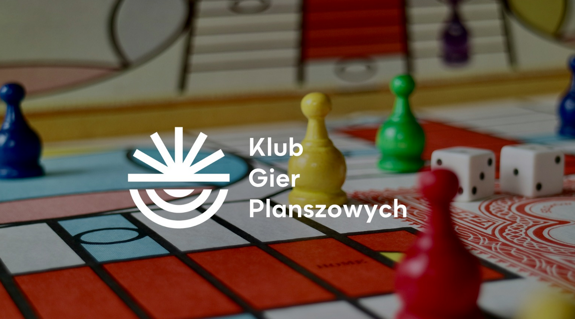 Pionki i kostki do gry planszowej rozstawione na planszy, na nich napis Klub Gier Planszowych i logo przypominające słońce