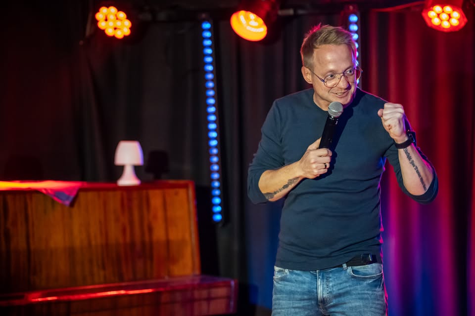 Mężczyzna występuje na scenie, trzyma mikrofon w ręku.