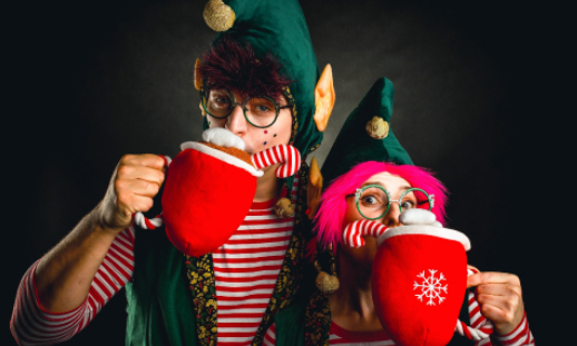 Dwoje aktorów w strojach elfów z dużymi pluszowymi, czerwonymi kubkami.