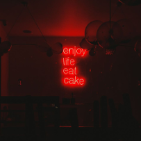 Świecący na czerwono neon-napis "Enjoy life eat cake".