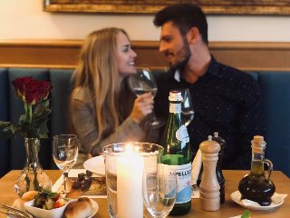 Zdjęcie, para siedzi przy zastawionym stole, świeca, kwiaty, butelka wina.