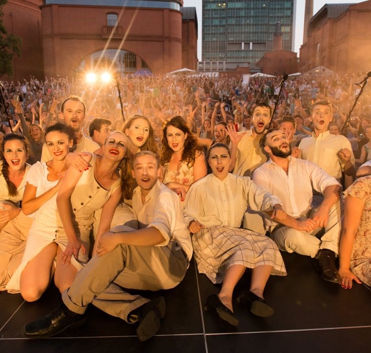 Grupa teatralna ubrana w kostiumy sceniczne pozuje do zdjęcia razem z widownią.