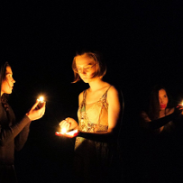 Trzy młode kobiety w ciemności zapalają zapałki, które oświetlają ich twarze. Każda patrzy w innym kierunku.
