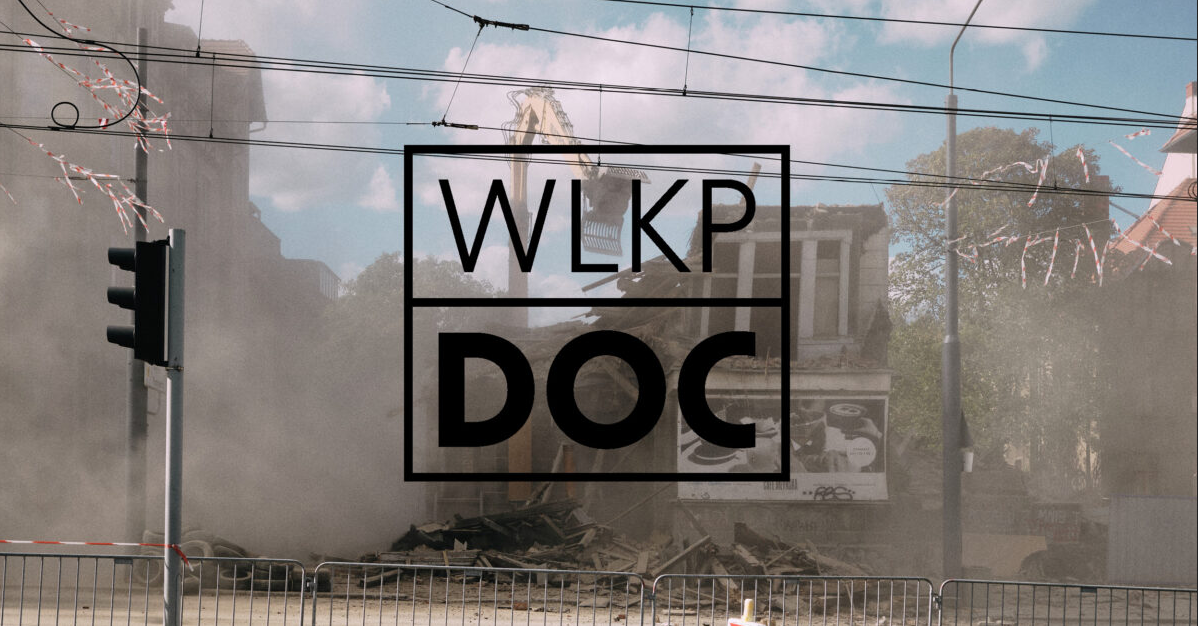Napis o treści wlkp doc, w tle zdjęcie wyburzanej kamienicy z widoczną rozwartą łyżką koparki i unoszącym się pylem.