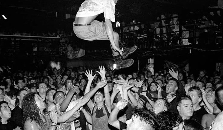 Czarno-białe zdjęcie zatłoczonego klubu, nad uczestników wyskakuje jeden z słuczaczy.