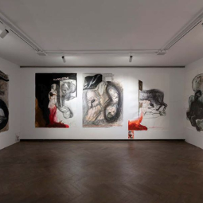 Wystawa "Anatomia polityczna". Pomieszczenie z trzema białymi ścianami, na których znajdują się obrazy operujące czernią, bielą i czerwienią