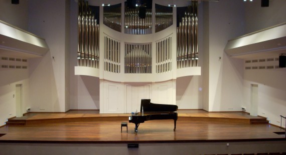 Na zdjęciu scena z fortepianem na środku. W tle piszczałki organów.