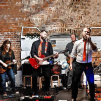 Na zdjęciu czteroosobowy zespół muzyczny na tle muru.