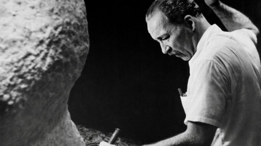 Na czarno-białym zdjęciu artysta rzeźbiący w kamieniu.