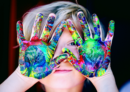 Twarz chłopca zasłaniają pomalowane róznymi kolorami ręce.