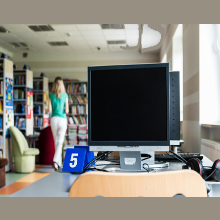 Na zdjęciu pomieszczenie biblioteczne. Na pierwszym planie stolik z komputerem, w tle regały z książkami.
