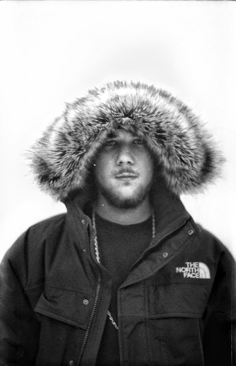 Na zdjęciu młody mężczyzna w zimowej kurtce z założonym na głowę kapturem.