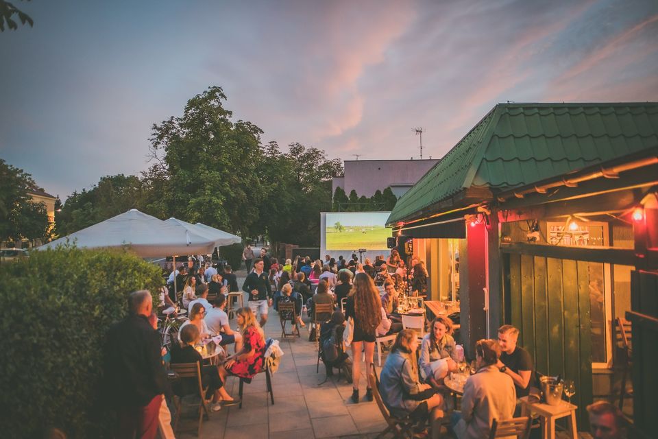 Ludzie siedzą wieczorem przy stolikach, rozmawiają.