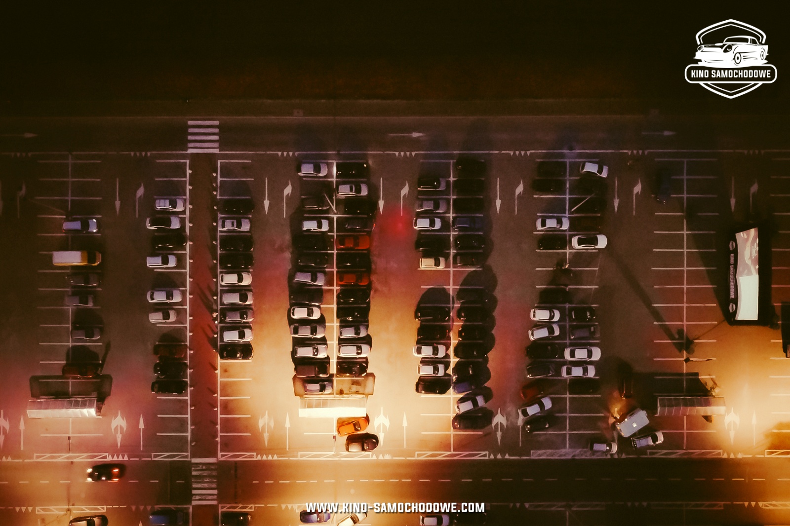 Parking z lotu ptaka, na nim samochody skierowane w stronę ekranu, na którym wyświetla się film.