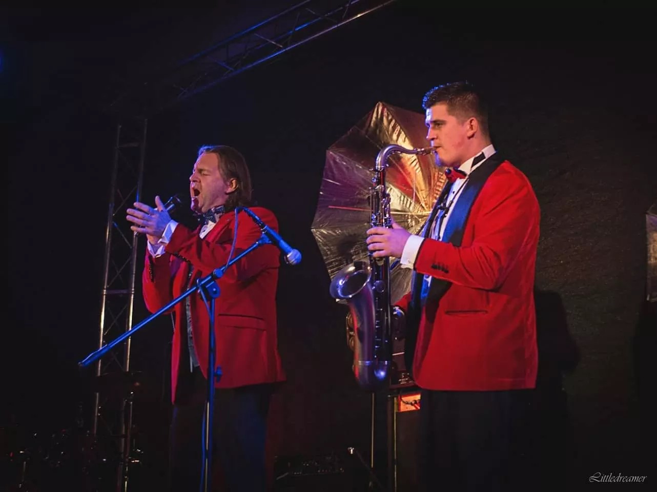 Dwójka mężczyzn. ubranych na czerwono, jedna śpiewa drugi gra na saksofonie.