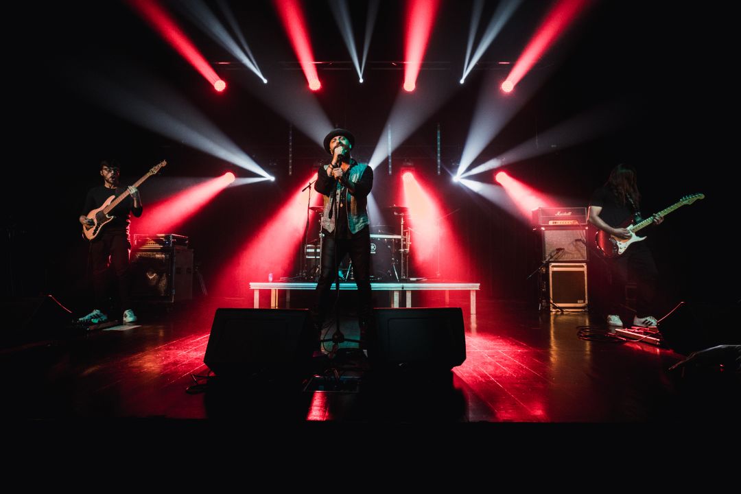 Na zdjęciu artysta śpiewający na scenie na tle czerwono białych świateł.