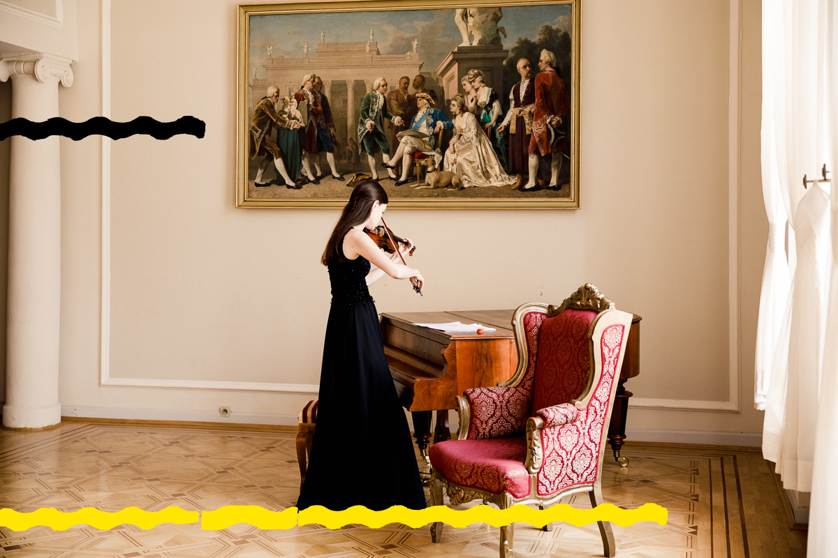Na zdjęciu skrzypaczka stojąca przy fortepianie. Na ścianie obraz przedstawiający scenę z życia dworu.