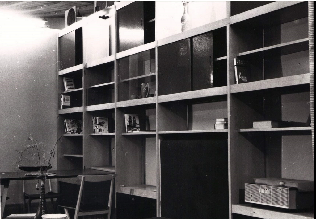 Czarno-białe zdjęcie drewnianej meblościanki. Na półkach widoczne są książki i stare radio.