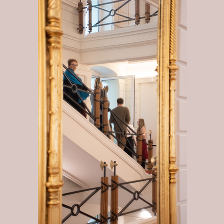 Grupa ludzi stoi na schodach Biblioteki i słucha przewodniczki.