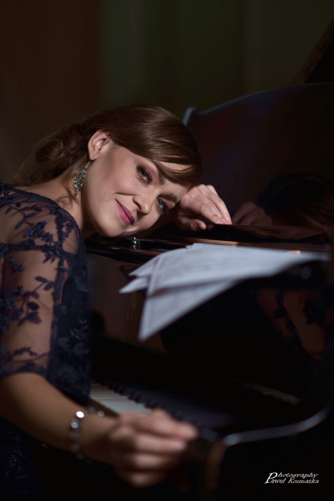 Na zdjęciu artystka opierająca twarz o fortepian.
