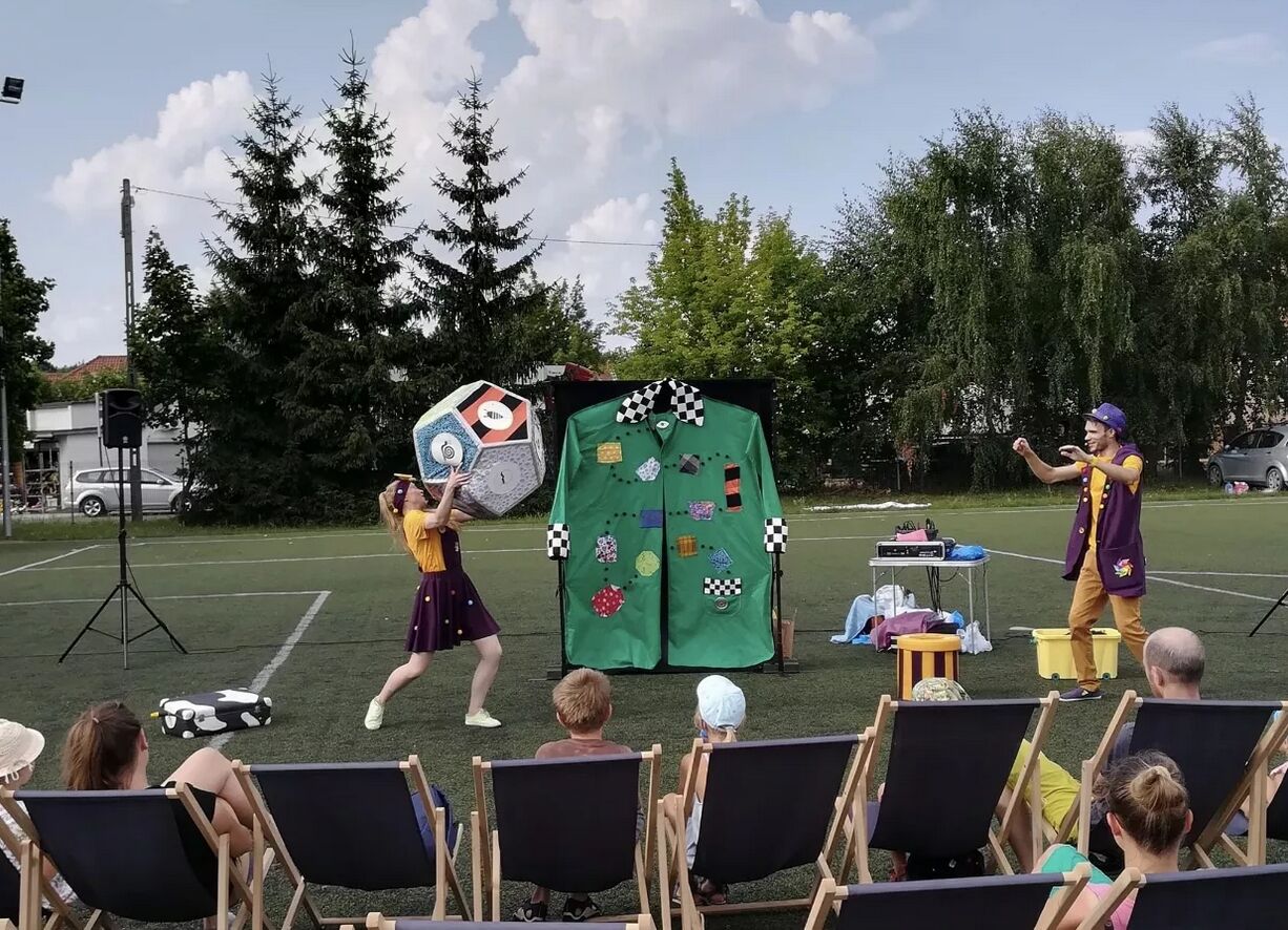 Kobieta i mężczyzna rzucający wielką kostką szcześcienną podczas zabawiania dzieci.