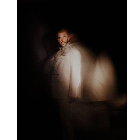 Rozmazana sylwetka artysty na ciemnym tle.